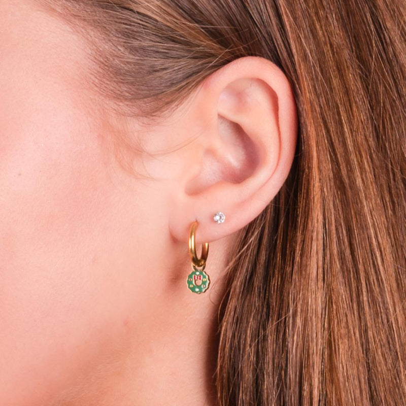 Close-up of a girl wearing a gold hoop earring with a green wreath charm.