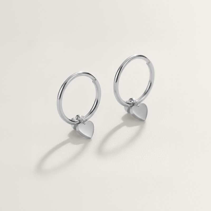 Mini heart huggie hypoallergenic hoop earrings in silver on white background