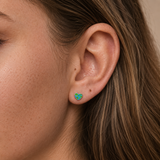 A close-up of a girl's ear wearing a small heart-shaped stud earring with a green and blue earth pattern.