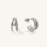 A pair of silver hoop earrings with clear crystal rhinestone detailing, shown from both side and back angles on a light cream background.