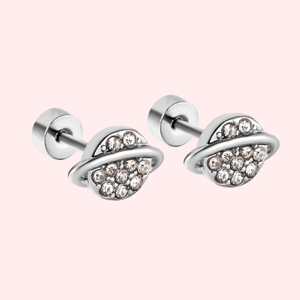 Silver planet-shaped earrings with embedded crystals on a light pink background.