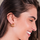 Close-up of a woman wearing gold hoop earrings with a neutral background.